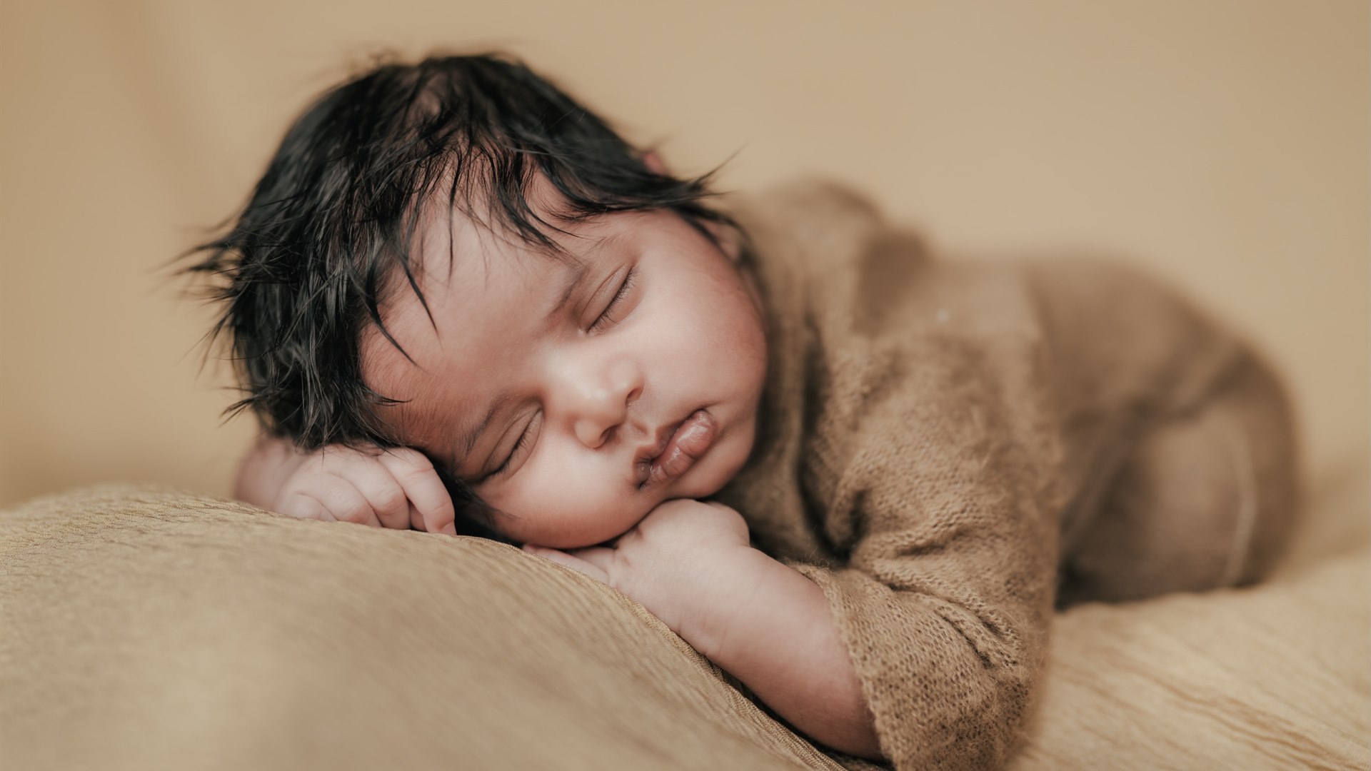 Newborn sleeping peacefully on a soft beige blanket