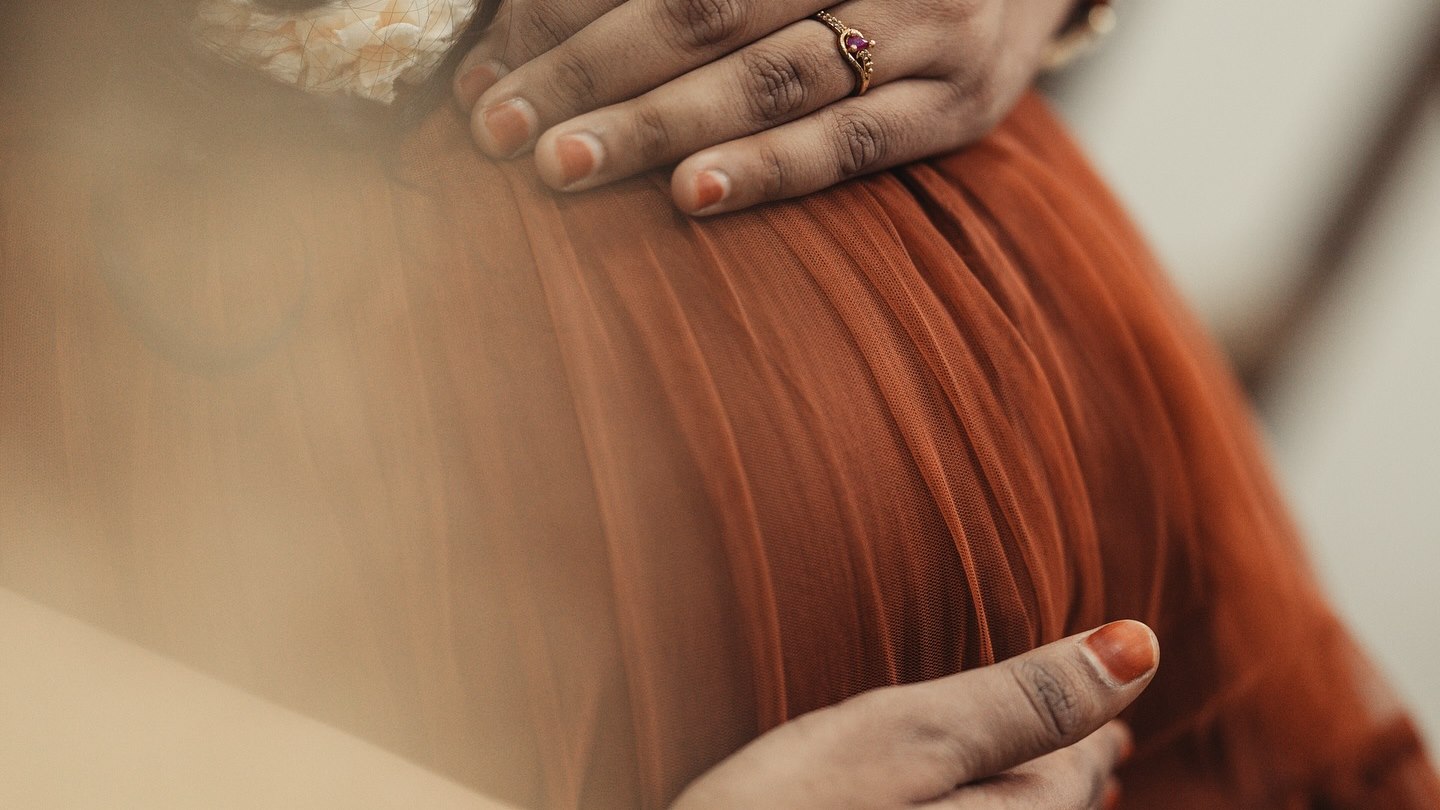 Hands resting on a pregnant belly, in warm light