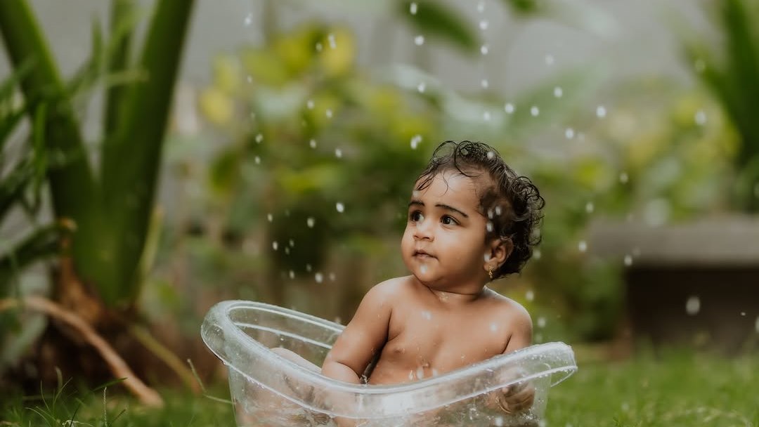 Toddler splashing in a tub under a big leaf in the garden